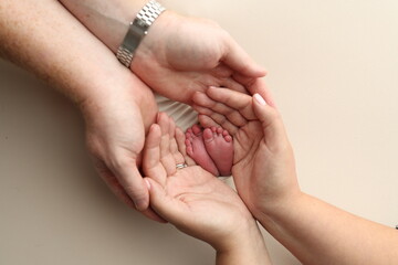 A father and mother hold the feet of a newborn child in a white blanket on a white background.. The feet of a newborn in the hands of parents. Photo of foot, heels and toes.The palms of the parents.
