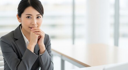 Fototapeta premium オフィスで手を組み笑顔を見せている、信頼感のある20代日本人女性社員