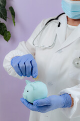The doctor holds a piggy bank in his hands and throws a coin.