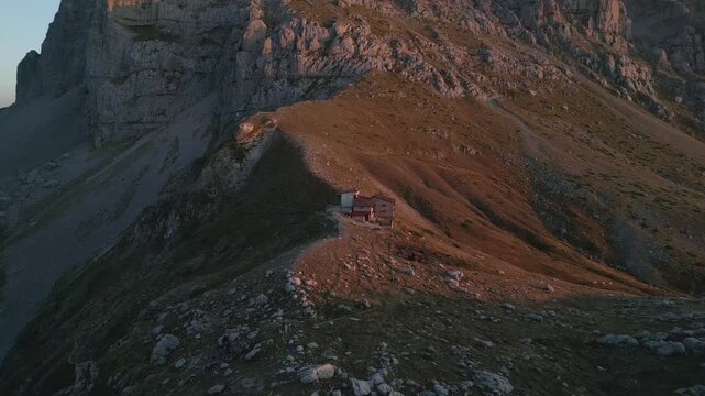 Drone footage of a refugee camp at Tymfi mountain during sunset. The camp is partially obscured, blending with the warm sunset light and surrounding mountains. Ideal for cinematic, documentary, travel