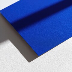 Close-up of a vibrant blue sheet of paper, angled on a white surface. A dramatic shadow falls across it