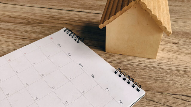Miniature Wooden House on Calendar Pages Illustrating Real Estate Deadlines, Mortgage Payments, and Closing Dates