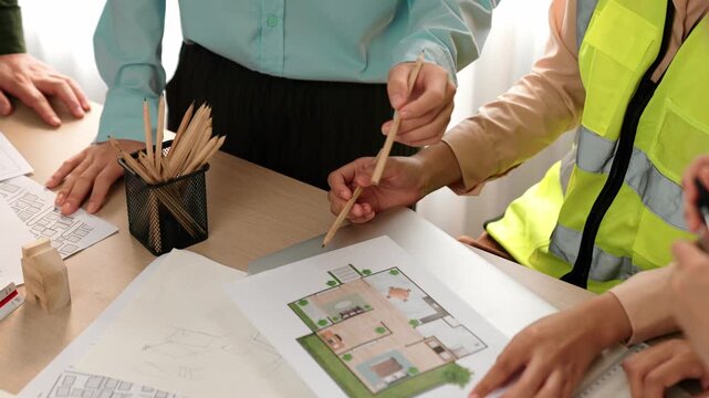 Smart architect and safety engineer discussion about building blueprint on table with architectural document, measurement tools and wooden block scatter around at modern office. Closeup. Delineation.