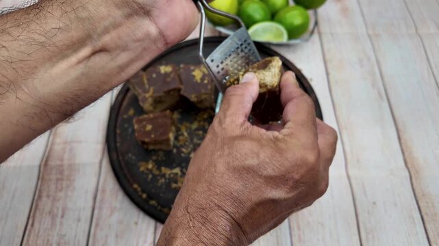 close-up shot hands-on, authentic process of grating a small block of hard panela (raw sugar cane) with a handheld metal grater, showing the texture of the ingredient and the manual labor