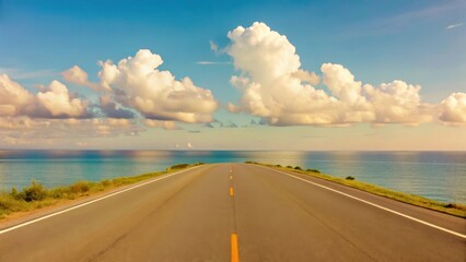 Fototapeta premium Scenic coastal road stretches towards azure ocean under bright sky with fluffy clouds