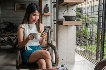 Woman sipping coffee while using smartphone in a stylish, industrial-themed cafe with natural light and cozy ambiance.
