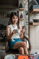 A young woman sits in a modern cafe, holding a coffee cup and smartphone, embodying a relaxed urban lifestyle.
