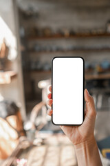 Close-up of a hand holding a smartphone with a blank screen, ideal for app or website mockup in a cozy home setting.