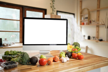 A mock up computer monitor The screen is blank sits on a wooden table with a variety of fruits and vegetables in front of it