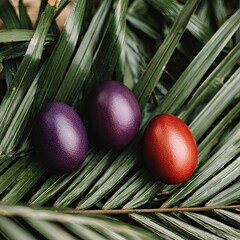 Three dyed eggs, purple and red, rest on textured, green tropical palm leaves