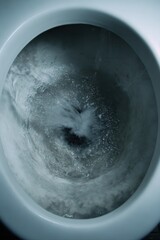 A close-up view of water swirling down a toilet bowl, capturing the motion and bubbles in a dark, moody setting.