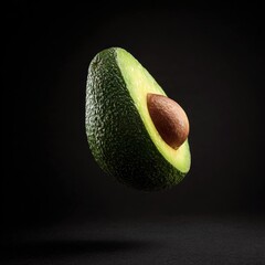 A halved avocado, suspended mid-air against a stark black backdrop. The seed is visible