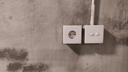 Minimalist electrical socket and switch mounted on a rustic concrete wall with stains and texture....