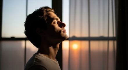 Serene young man enjoying sunrise with closed eyes indoors