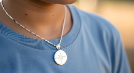 Close-up of a stylish silver necklace featuring an intricate compass rose pendant, elegantly worn by a person in a soft blue t-shirt, symbolizing personal guidance and journey