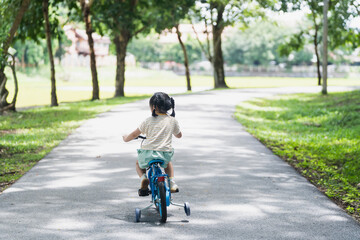 Obraz premium Young child riding tricycle on pathway in serene park surrounded by trees, sunlight filtering through leaves, joyful outdoor experience, childhood adventure