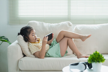 Young girl relaxing on couch using smartphone while listening to music with headphones in bright living room space with natural light