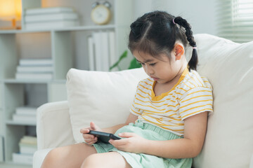 Young girl sitting on a couch focused on mobile device, engaging with technology in cozy living room, showcasing childhood and modern lifestyle