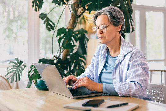 Focused mature woman working on freelance laptop project in cozy modern workspace with natural light