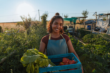 Young farmer woman holding crate of vegetables in her garden