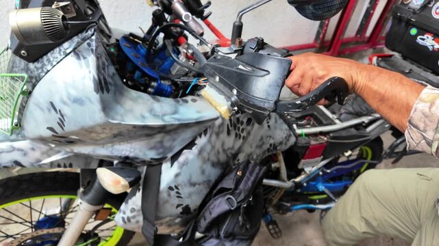 Pulling back from a mechanic's hands performing preventative maintenance on a white camouflage adventure motorcycle.