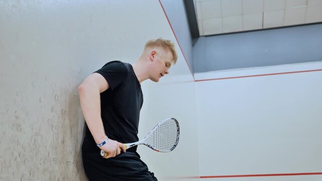 Tired squash athlete rests on court wall after heated indoor match with sweat
