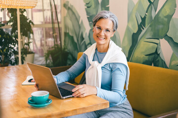Confident senior freelancer working remotely on laptop, smiling in green-themed modern workspace