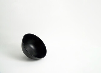 A simple, empty black bowl is tilted on a clean white background. Its minimalist design and dynamic angle make it perfect for adding text or other elements, suitable for themes of cooking, simplicity
