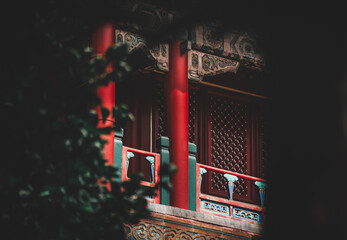 View of The Palace Museum, Beijing. Architectural details peek through foliage. Red columns and...