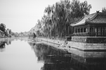 A serene monochrome view of The Palace Museum, Beijing. Reflective water mirrors the traditional...