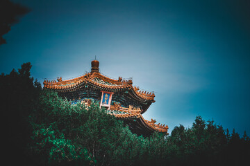 Majestic architecture emerges from lush greenery against a dramatic sky at The Palace Museum,...