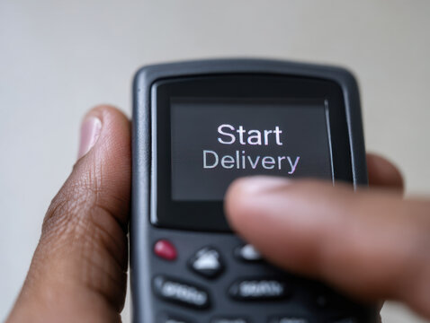 Start delivery button on handheld device with workers organizing parcels for efficient shipment and logistics management - Powered by Adobe