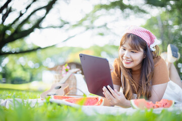 Young woman enjoys leisure picnic outdoors using tablet with family concept in mind surrounded by nature and fresh watermelon slices creating happy and relaxed mood