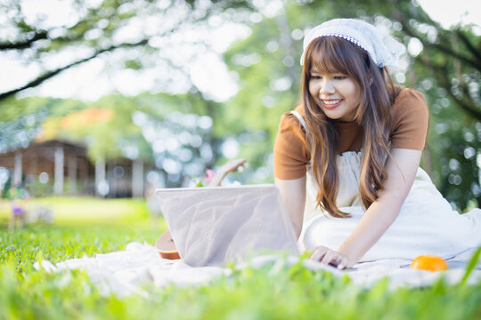 Young woman enjoys leisure time on picnic blanket using laptop outdoors surrounded by nature, capturing concept of people spending quality family moments in park