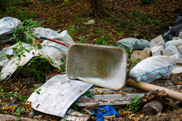A discarded construction wheelbarrow at an illegal dump near the forest