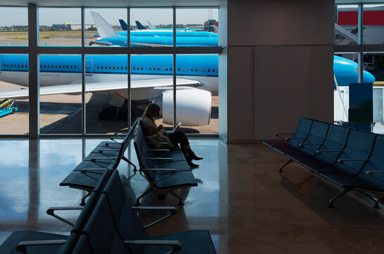 Amsterdam Airport Schiphol. Schiphol is the main international airport of the Netherlands - Silhouette of young woman working on laptop and waiting for flight in the Airport