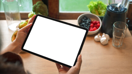 Hands holding digital tablet with blank screen in kitchen surrounded by healthy ingredients and blender