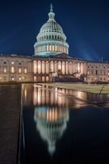 The illuminated U.S. Capitol Building in Washington D.C. at night with a reflection in a small puddle