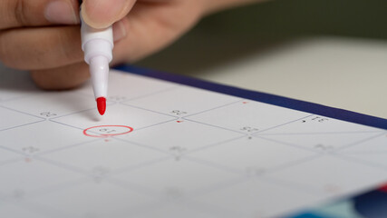 Close up of hand circling date on calendar with red marker, symbolizing appointment, or reminder