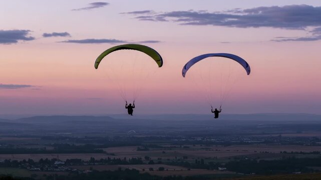 Two paragliders soaring in the sky at sunset with a scenic landscape below