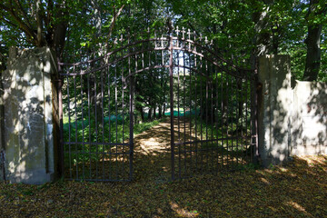 ​An open, wrought iron metal gate with a decorative top stands between two massive stone pillars,...