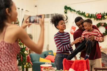 Black woman using smartphone taking picture of an African family during Christmas celebration at home. Decoration background, people gathering on winter holiday and doing activities together