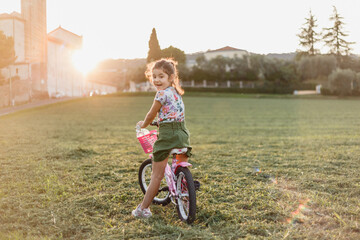 rear view of a small girl riding pink bicycle outdoors during sunset