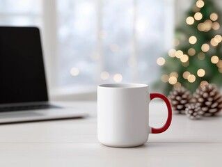 Fototapeta premium White ceramic mug with red handle placed on wooden table, laptop in background, decorated Christmas tree with lights and pine cones creating a cozy holiday atmosphere