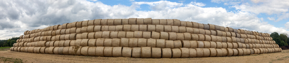 Large stack of hay bales arranged in a pyramid on a countryside landscape