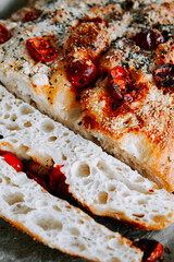 Freshly baked focaccia bread topped with cherry tomatoes and herbs on a wooden table