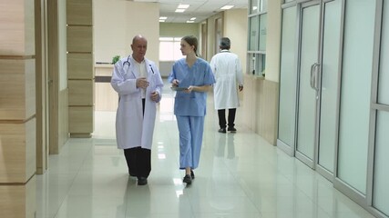 Hospital, healthcare, medical, doctor, nurse using tablet to review patient information, senior male mentoring young student trinee in hallway, technology helps improve teamwork efficiency diagnosis - Powered by Adobe
