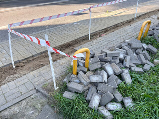 Pile of gray concrete paving blocks stacked beside a taped-off sidewalk repair area
