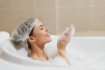 Relaxed young woman enjoying a bubbly bath, smiling while playing with foam. Spa and self-care concept with calming atmosphere.