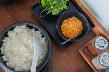 Top view of bowl with boiled rice with ladle, fried garlic and Chinese chives